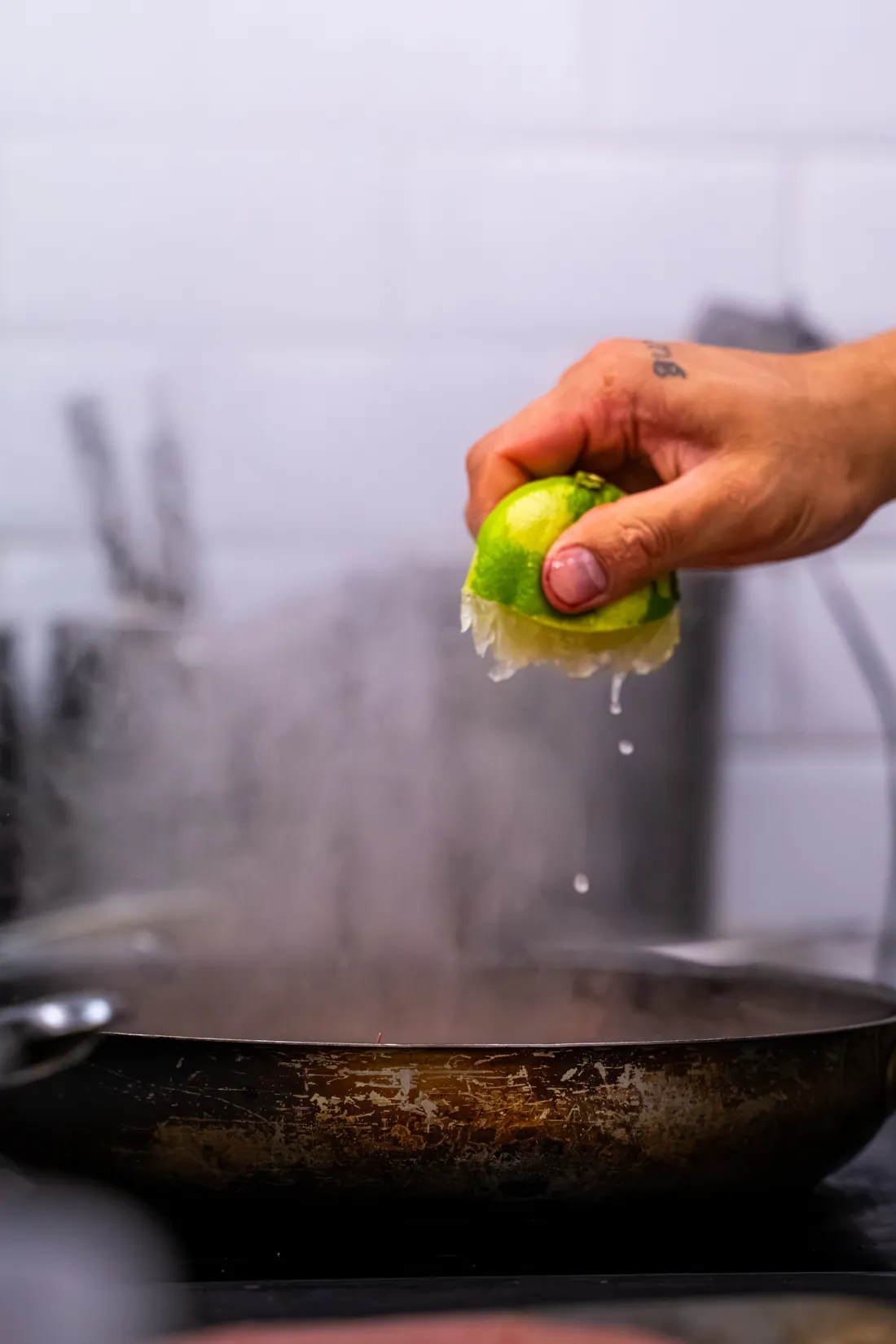 A hand squeezes lime over a pan